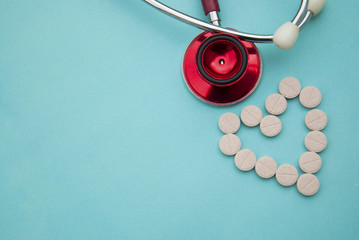 Red stethoscope with tablets, pills on blue background. Copy space. Medicine, heartbeast concept.