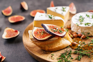 Tasty sandwich with ripe fig and brie cheese on wooden plate, closeup