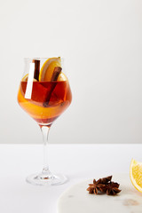 close up view of tasty mulled wine with orange pieces and anise stars on white tabletop on grey background