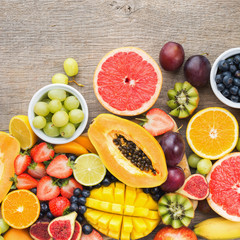 Overhead view of colorful fruits, strawberries blueberries, mango orange, grapefruit, banana papaya apple, grapes, kiwis on the grey wood background, copy space for text, selective focus
