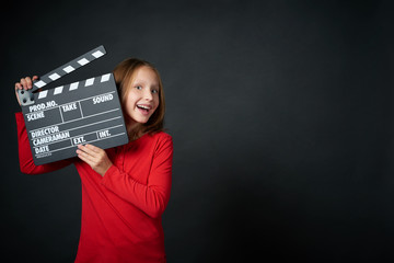 Happy smiling girl holding clap board, over dark background