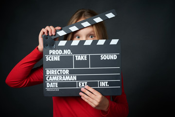Happy smiling girl holding clap board peeping, over dark background