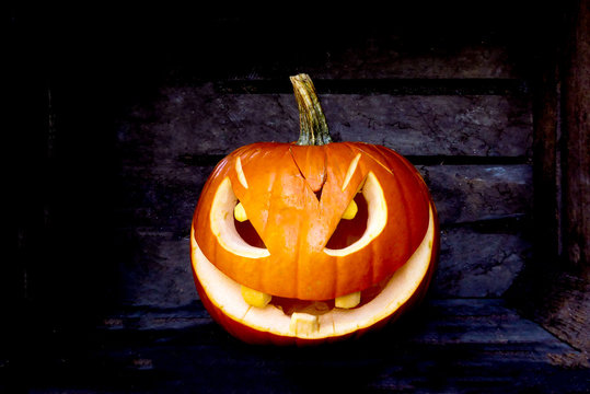 image of Halloween pumpkin scary face lay down on a wooden block in the dark.