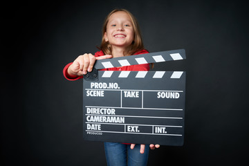 Happy smiling girl holding clap board, over dark background. Shallow depth of field, focus on...