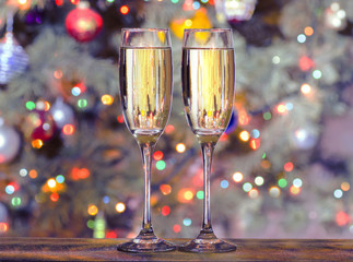 Christmas glasses with champagne on the background of the Christmas tree with toys decorated with colorful lights