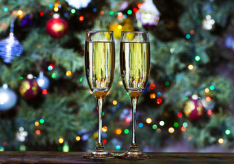 Christmas glasses with champagne on the background of the Christmas tree with toys decorated with colorful lights