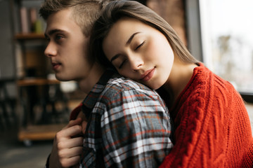 Close up portrait of young beautiful family in loft modern apartments. Beautiful woman hugging her husband at cozy home. Lovely couple together sitting near window. 