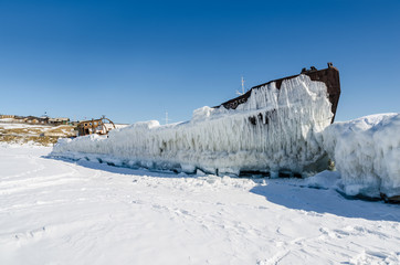 Old iron ship covered with ice at lake in winter