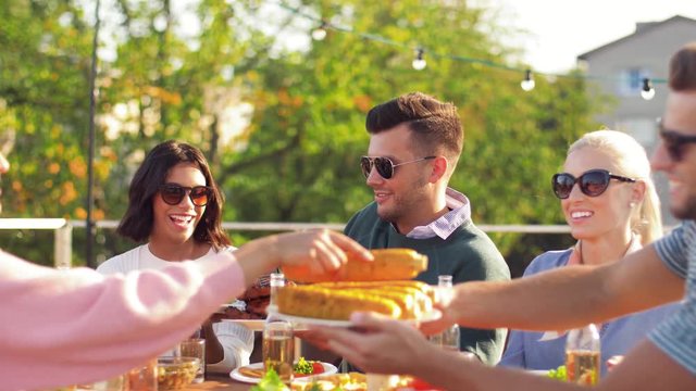 leisure and people concept - happy friends eating and drinking at rooftop party in summer