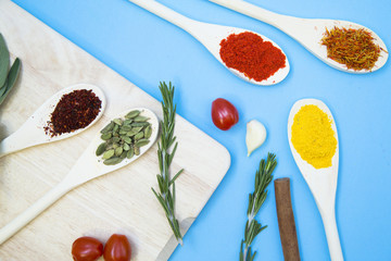 Dry spices, beans and herbs in wooden spoons on a wooden cutting board, light blue background