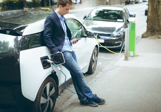 Businessman using mobile phone while charging electric car