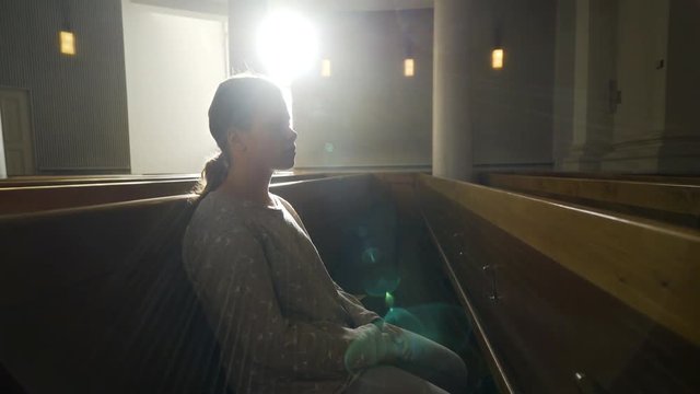 Close-up view of young woman in back lit. Woman praying in dark cathedral in bright sun shine from window