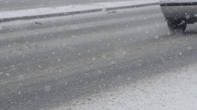SLOW MOTION, CLOSE UP: Morning traffic drives down the slippery asphalt road during a dangerous blizzard. Cars leaving trails in the dirty snow gathering on the slick surface of the concrete highway.