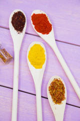 Cooking Hot Spicy Food Concept. Dry spices,beans and herbs in plastic cup, glass jar with cork and wooden spoon, purple wooden background