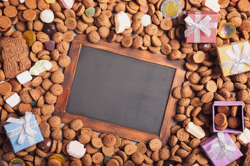 Dutch holiday Sinterklaas background with black chalkboard, gifts, pepernoten, traditional sweets strooigoed. Flat lay and copy space.