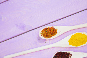 Cooking Hot Spicy Food Concept. Dry spices,beans and herbs in plastic cup, glass jar with cork and wooden spoon, purple wooden background