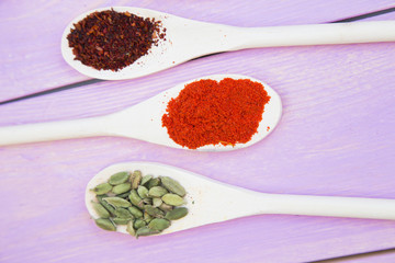Cooking Hot Spicy Food Concept. Dry spices,beans and herbs in plastic cup, glass jar with cork and wooden spoon, purple wooden background