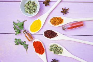 Cooking Hot Spicy Food Concept. Dry spices,beans and herbs in plastic cup, glass jar with cork and wooden spoon, purple wooden background
