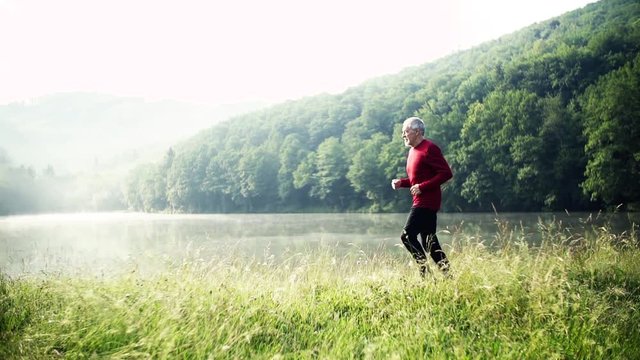 Senior man running by the lake outdoor in the morning in nature.