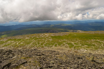 Landscape of green valley flooded with light with lush green grass, mountains, covered with stone and hills, a fresh summer day under a blue sky with white clouds and sun rays in Altai mountains
