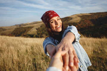 Happy young woman holds the hand of a man in nature