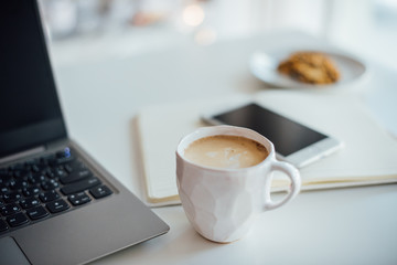 Modern white office, designer handmade cup with coffee, smartpho