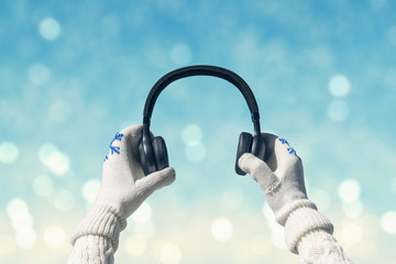 Female hands in the winter mittens with a headphones on the winter blurred snowfall  background....
