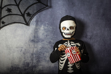 Little kid in a skeleton costume eating fake eyes on Halloween