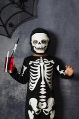 Little kid in a skeleton costume drinking  fake blood on Halloween