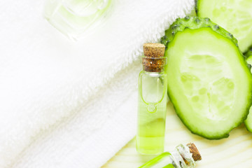 Obraz na płótnie Canvas Cucumber home spa and hair care concept. Sliced cucumber, bottles of oil, jar of mask, bathroom towel. White board background