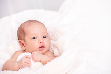 Little cute newborn girl wrapping by white fur blanket looking at camera on white bed.