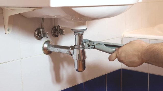 plumber fixes two adjustable pipe wrenches on sink siphon