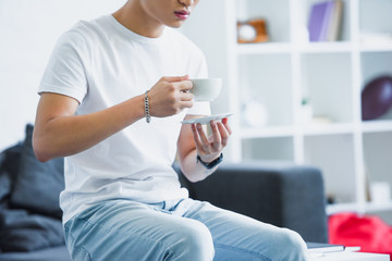 cropped image of man sitting on table with cup of coffee in morning at home