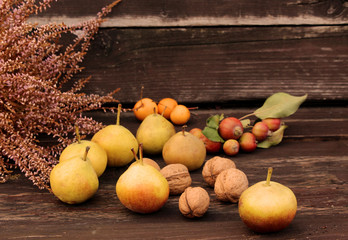 Autumn styled botanical arrangement. Composition of little apples and little pears,walnuts and erica on wooden table background. Fall decorative concept.