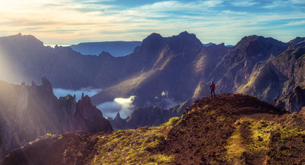 Madeira, Portugal. Man taking photograph on a hiking path between Pico do Arieiro and Pico do Ruivo at sunset above the clouds - obrazy, fototapety, plakaty