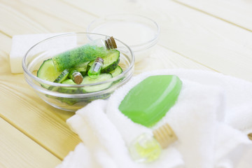 Cucumber home spa and hair care concept. Sliced cucumber, bottles of oil, soap, jar of mask, bathroom towel. White board background