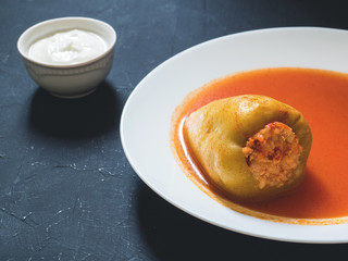 Stuffed pepper in a white plate with sour cream on a black background