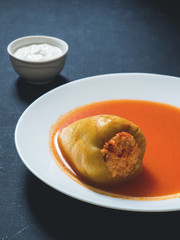 Stuffed pepper in a white plate with sour cream on a black background