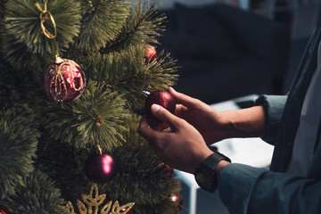 close-up partial view of young man decorating christmas tree at home
