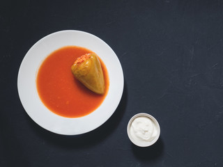 Stuffed pepper in a white plate with sour cream on a black background. Flat lay, top view, copy space