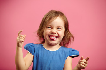 Portrait of joyful little girl in good mood, bit her tongue, raised hands up.