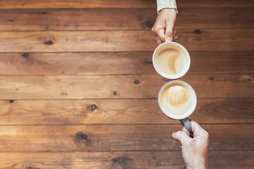 Male's and female's hands with an cup of coffee on the wooden table background. Winter concept