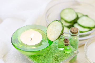 Obraz na płótnie Canvas Cucumber home spa and hair care concept. Sliced cucumber, bottles of oil, sea salt, bathroom towel. White board background