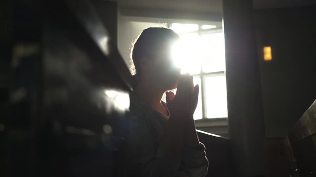 Crop side view of young woman with eyes closed holding hands together and worshiping in cathedral