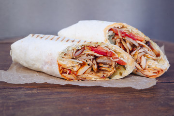 Shawarma sandwich gyro- fresh roll of thin lavash (pita bread) filled with grilled meat, mushrooms, cheese, cabbage, carrots, sauce, green. Traditional Eastern snack. On a wooden background