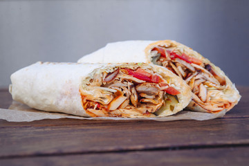 Shawarma sandwich gyro- fresh roll of thin lavash (pita bread) filled with grilled meat, mushrooms, cheese, cabbage, carrots, sauce, green. Traditional Eastern snack. On a wooden background