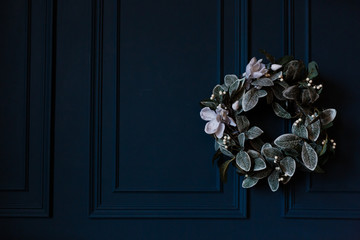 Christmas wreath with leaves and white flowers on dark blue wall