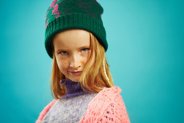 portrait of beautiful child girl in winter sweater and hat on blue isolated.