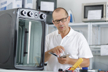 Naklejka na ściany i meble repairman using phone to fix domestic oven in kitchen