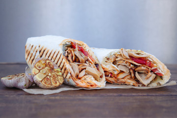 Shawarma sandwich gyro- fresh roll of thin lavash (pita bread) filled with grilled meat, mushrooms, cheese, cabbage, carrots, sauce, green. Traditional Eastern snack. On a wooden background